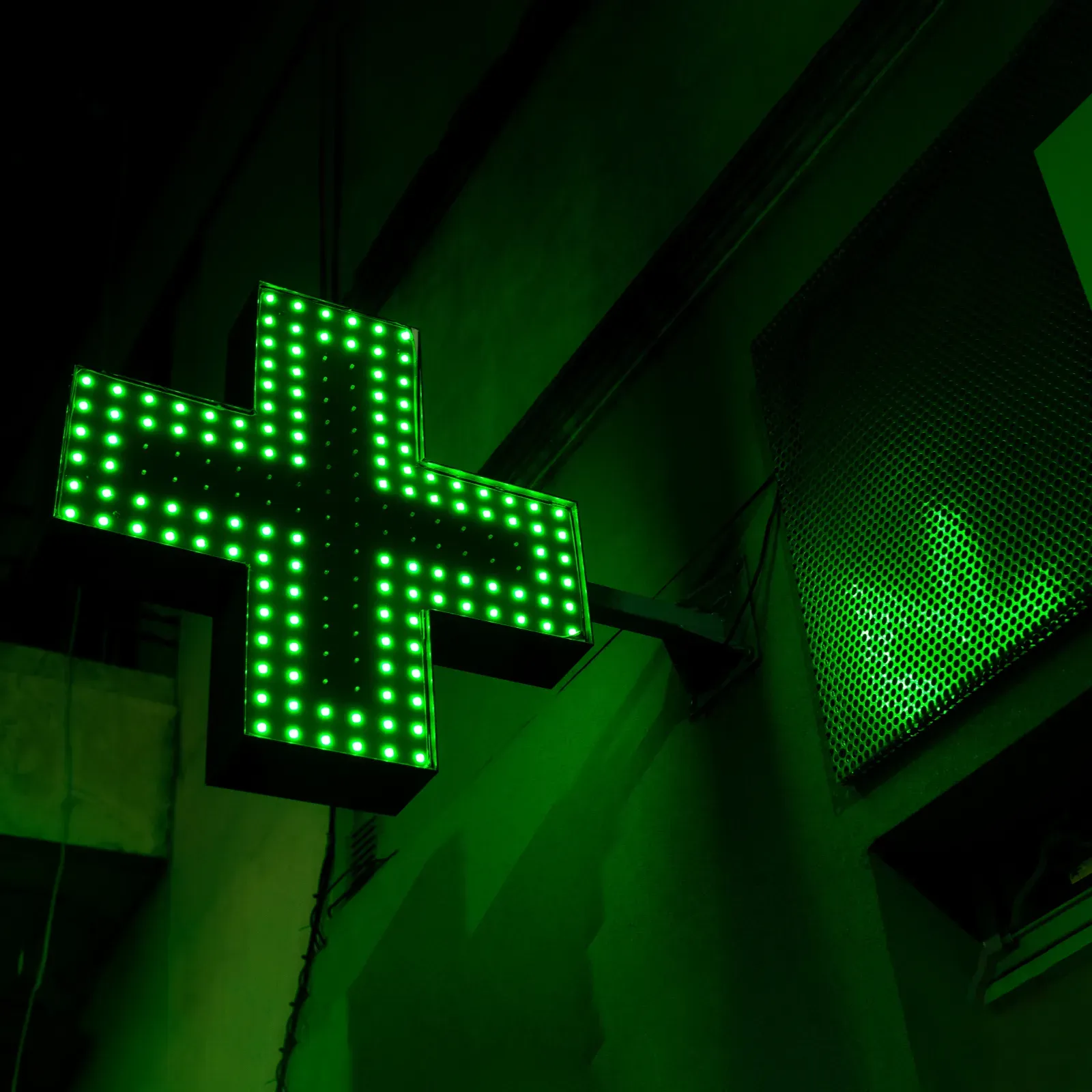 Illuminated green pharmacy cross at night